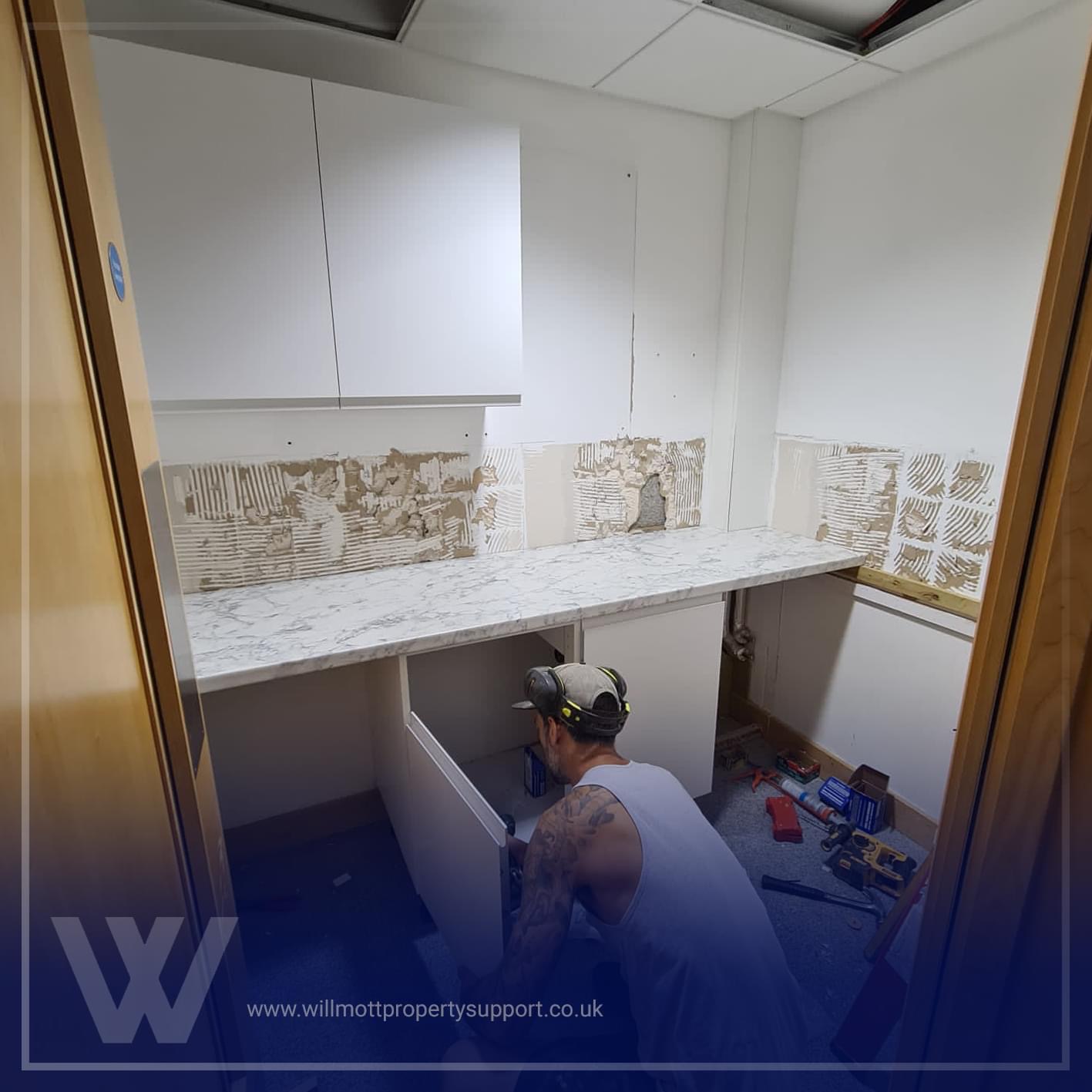 Tradesman kneeling down fitting a new kitchen cabinet
